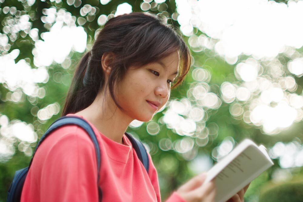 Teens - girl reading outside, wearing a backpack
