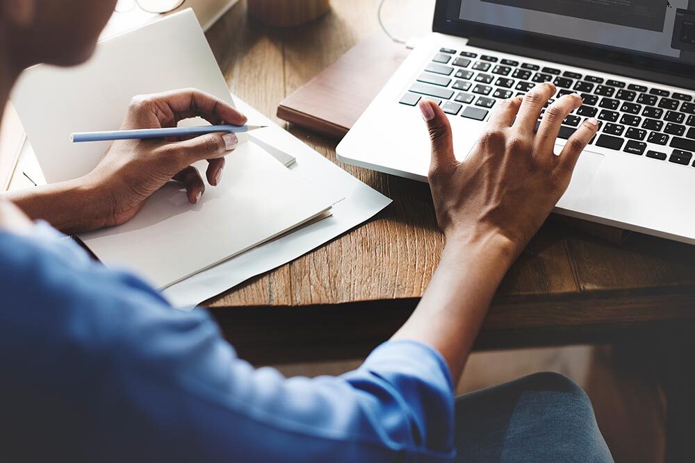 Writer in Residence - unrecognizable person with hands using a laptop keyboard and notebook with a pen