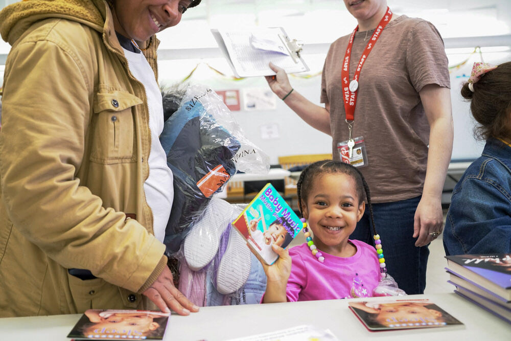 smiling child holding a free bilingual book and free clothing during Operation Warm