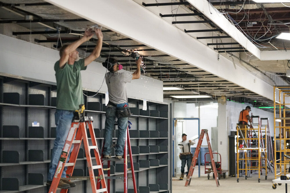 Pratt Library renovations - workers on ladders and empty bookshelves