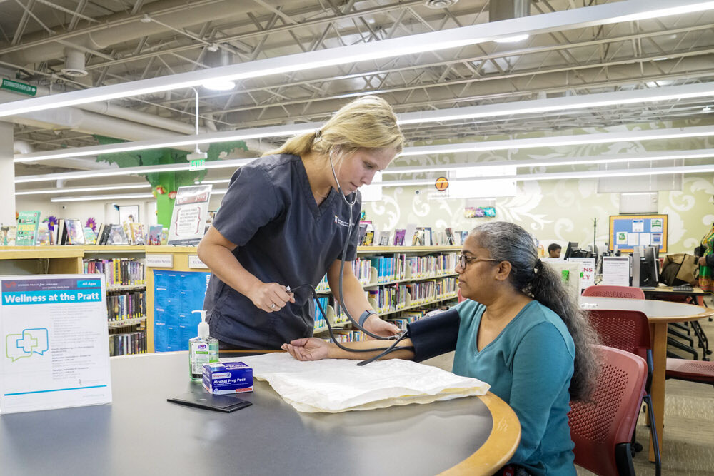 Wellness at the Pratt - a nurse taking a woman's blood pressure in the library