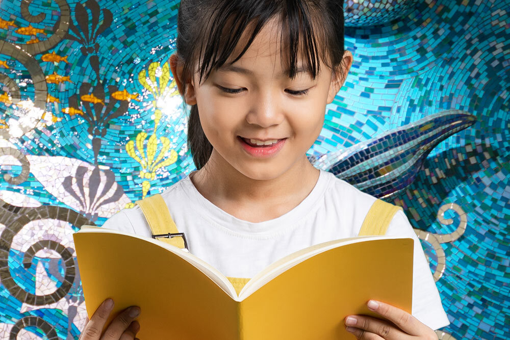 Read to Reef book club for kids - child reading a book by a fish-themed mosaic wall