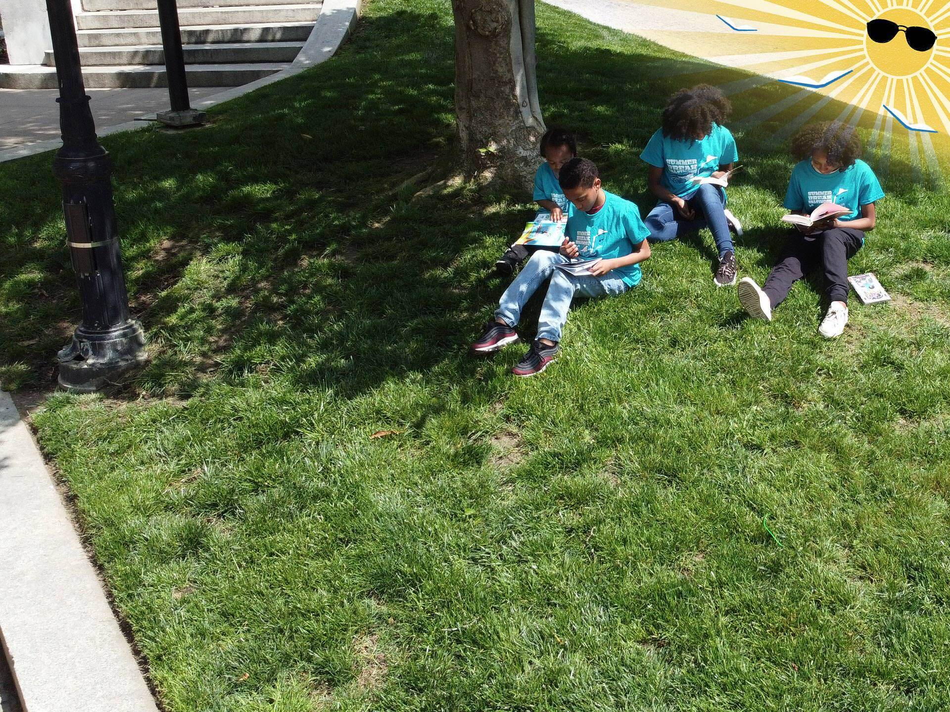Summer Break 2024 - a family all reading books and wearing the 2024 t-shirt by a tree