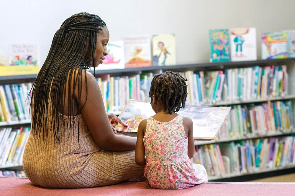 Photo from behind showing an adult and child reading a book together