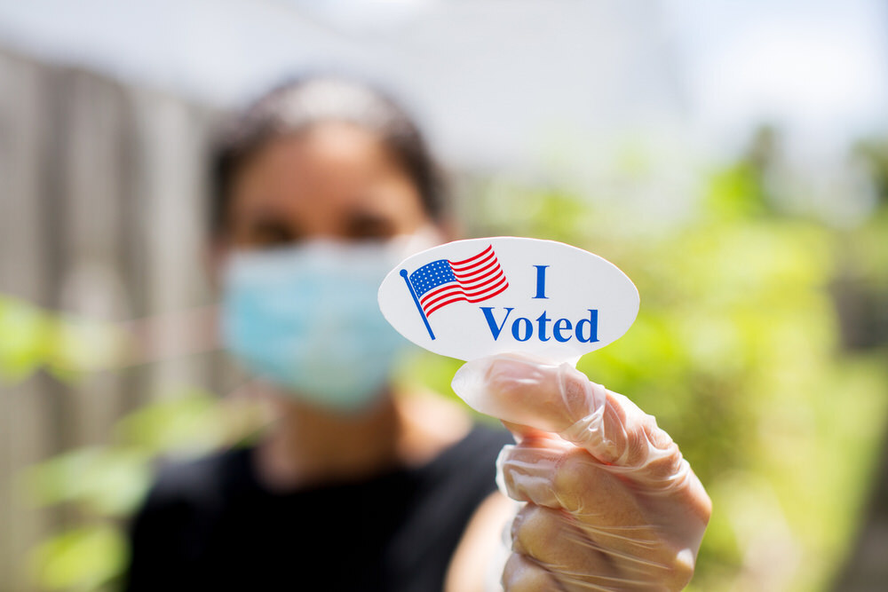 Photo of a woman holding up an "I Voted" sticker