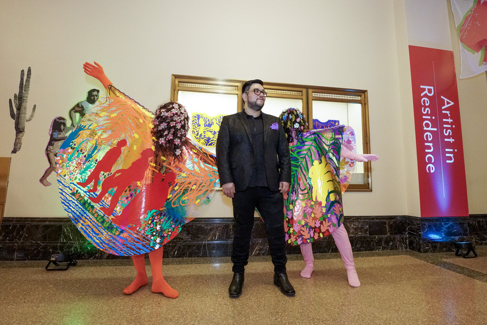 Artist in Residence Hoesy Corona with sign and dancers in climate ponchos