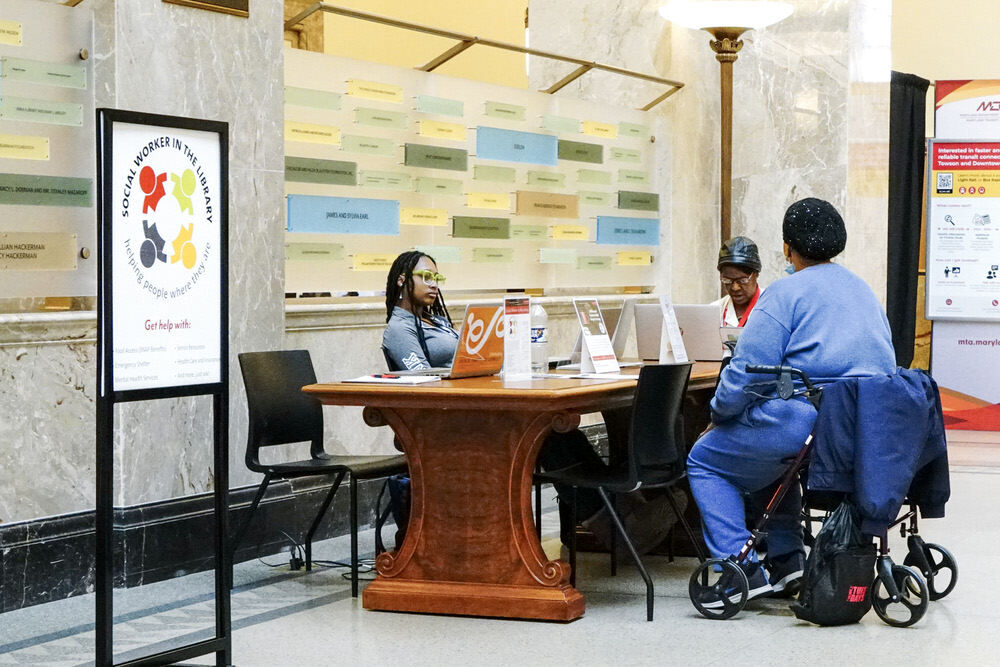 Social Worker in the Library sign by a table with customer and social workers