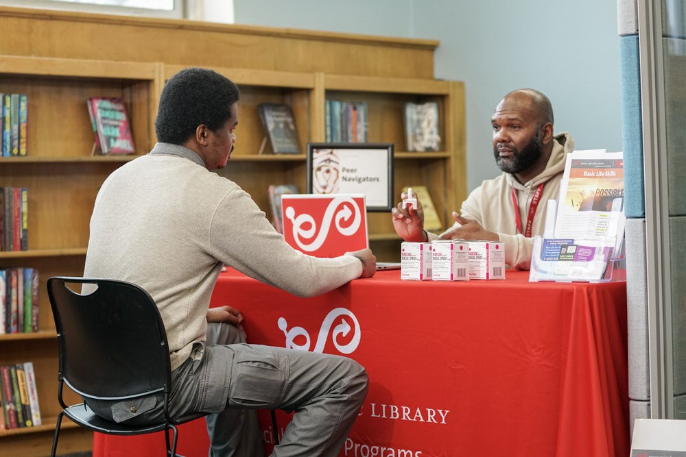 Peer recovery table with two men and narcan at the library