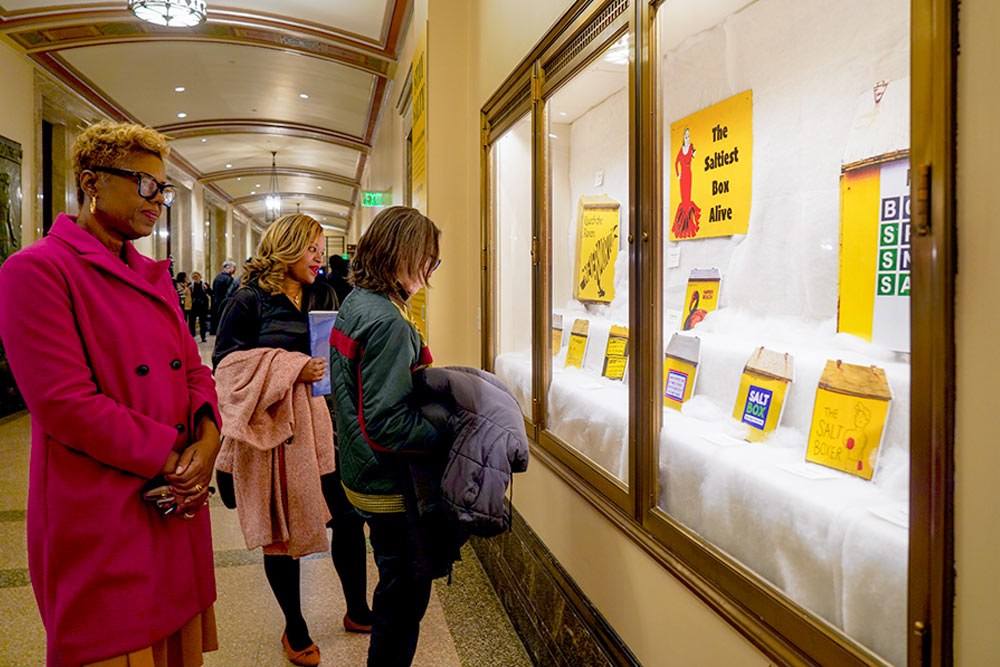 Salt Box exhibit - people looking at display windows in a wall case showing various cutouts of salt box designs